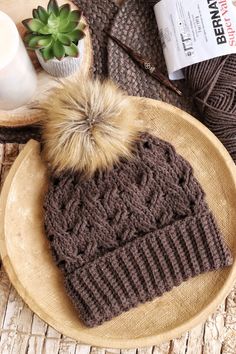 a knitted hat with a fur pom sits on top of a wooden bowl