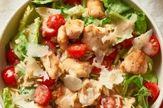 a salad with chicken, tomatoes and lettuce in a white bowl on a table