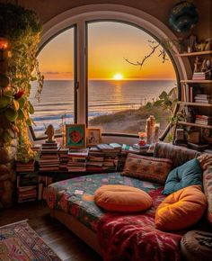 a living room filled with furniture and a large window overlooking the ocean at sunset or sunrise