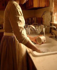 a woman washing dishes in a kitchen sink with a paper towel on the counter top