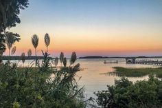 the sun is setting over the water and there is a dock in the distance with trees on both sides