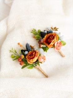 two boutonnieres with flowers on them sitting on a white cloth covered surface