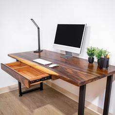 a wooden desk with a computer monitor and keyboard on it, in front of a white wall