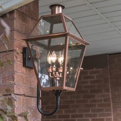 an outdoor light hanging from the side of a brick building with lights on it's sides