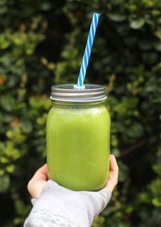 a hand holding a green smoothie with a blue striped straw