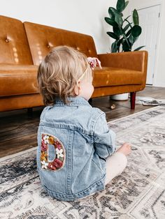 a toddler sitting on the floor in front of a couch and looking at something