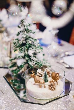 a table topped with a glass bowl filled with snow covered trees and reindeer figurines