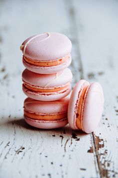 a stack of pink macaroons sitting on top of a white wooden table next to each other