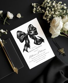 a black and white wedding card with a bow on it, surrounded by flowers in the background