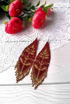 two red beaded earrings sitting on top of a white table next to pink flowers