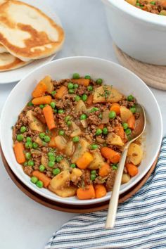 a bowl filled with meat and vegetables next to pita bread on a table top