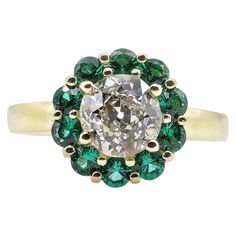 an oval cut diamond surrounded by emeralds and yellow gold accents, set in a flower - shaped setting