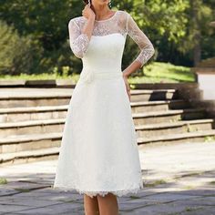 a woman in a white dress is talking on her cell phone while standing near steps