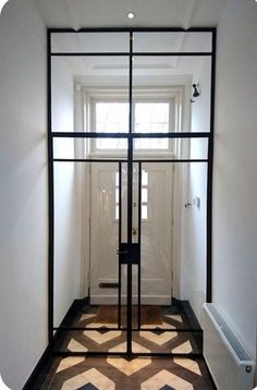 an empty hallway with white walls and black glass doors on the door, in front of a window