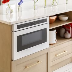 a kitchen with white counter tops and wooden cabinets, flowers in vases on the shelf