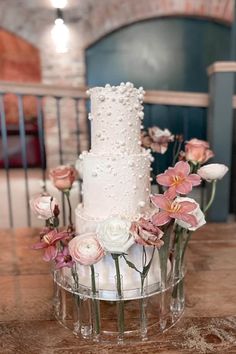 a three tiered white wedding cake with pink and white flowers on the bottom layer