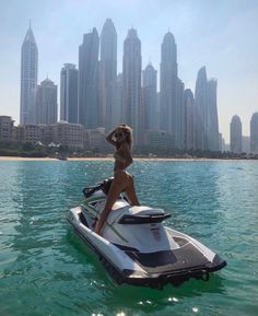 a woman riding on the back of a white and black jet ski in front of a city skyline