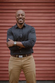 a man standing in front of a red wall with his arms crossed and looking at the camera