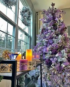 purple and white flowers are on display in front of a large window, surrounded by candles