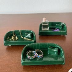 three green trays with rings and other items on them sitting on a wooden table