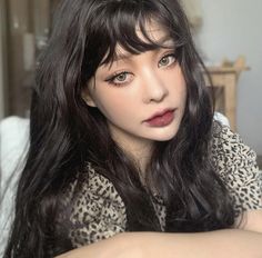 a woman with long black hair and leopard print shirt sitting on a bed looking at the camera