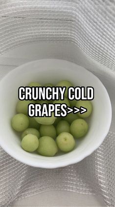 a white bowl filled with green grapes sitting on top of a cloth covered tablecloth