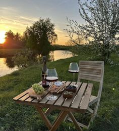 two glasses of wine and some food on a wooden table near the water at sunset