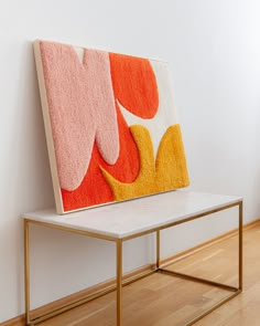 an orange and pink painting sitting on top of a table next to a white wall