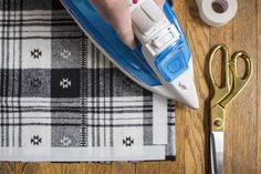 a person ironing fabric with scissors on a wooden table next to some tape and thread