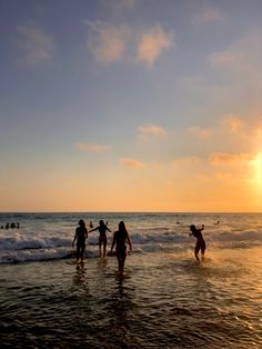 several people are wading in the ocean at sunset