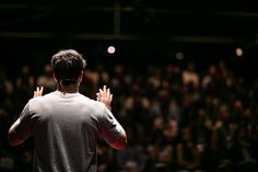 a man standing in front of an audience with his hands up to the side,