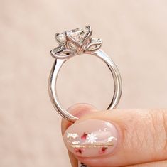 a woman's hand holding a diamond ring with flowers on the band and pink nail polish