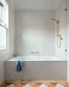 a bath tub sitting next to a window in a bathroom with tiled floors and walls