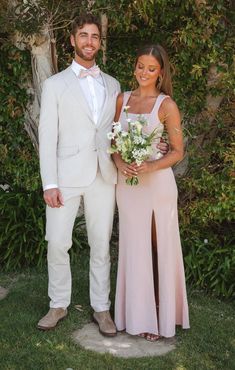 a man and woman standing next to each other in front of some bushes with flowers