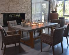 a dining room table with candles on it and wicker chairs around it, in front of a fireplace