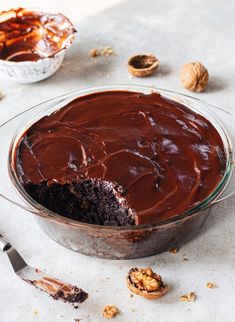 a chocolate cake in a glass dish with one slice taken out and walnuts on the side