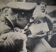 an old black and white photo of a man in uniform signing autographs for people