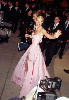 a woman in a pink dress walking down the street with people behind her and cameras around her