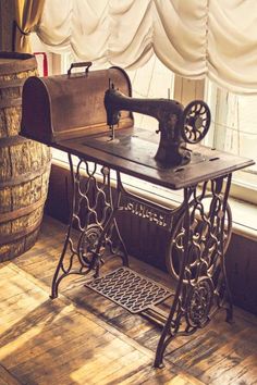 an old fashioned sewing machine sitting on top of a wooden table next to a window