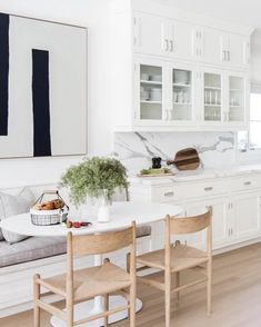 a kitchen with white cabinets and marble counter tops is pictured in this image, there are two wooden chairs at the table