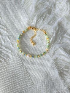 a gold bracelet with beads and a cross on it, sitting on a white blanket