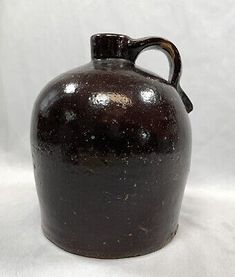 an old black jug is sitting on a white surface