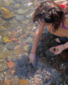 a woman kneeling down in the water with her hand on some rocks and looking at something