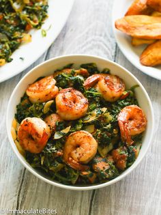 a bowl filled with shrimp and spinach next to some french fries on the side