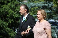 a man in a suit and tie walking next to a woman wearing a pink dress