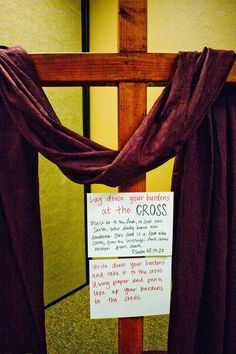 a wooden cross with a sign hanging on it's side in front of a wall