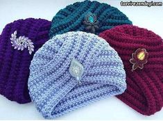 three knitted beanies with flowers on them are laying next to each other and one has a brooch