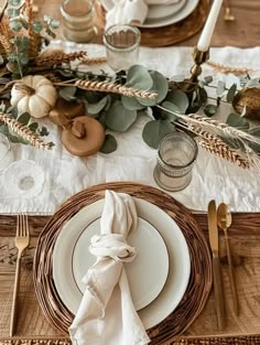 the table is set with white plates, silverware and greenery on top of it