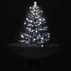 a lit up christmas tree on top of a black table with white balls and snowflakes