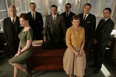 a group of people in suits and ties posing for a photo on a wooden desk